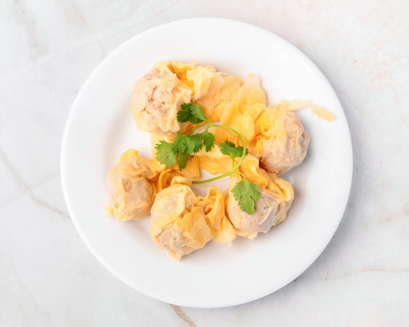 A white plate holds several steamed wontons, garnished with fresh green cilantro.