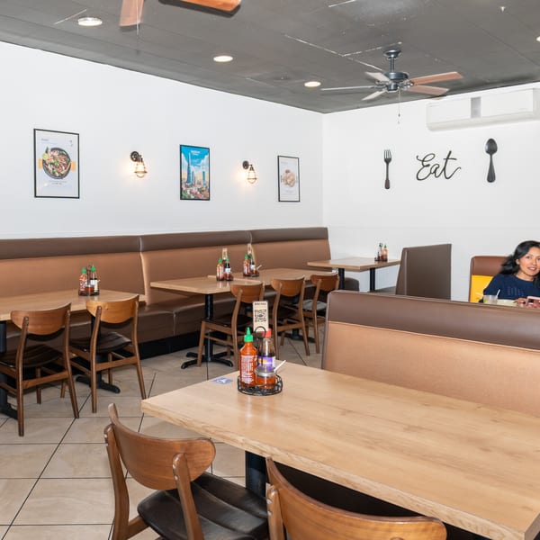 A restaurant interior with brown booths, wooden tables, and a woman and child eating in the background.