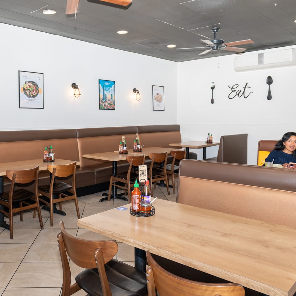 A restaurant interior with brown booths, wooden tables, and a woman and child eating in the background.