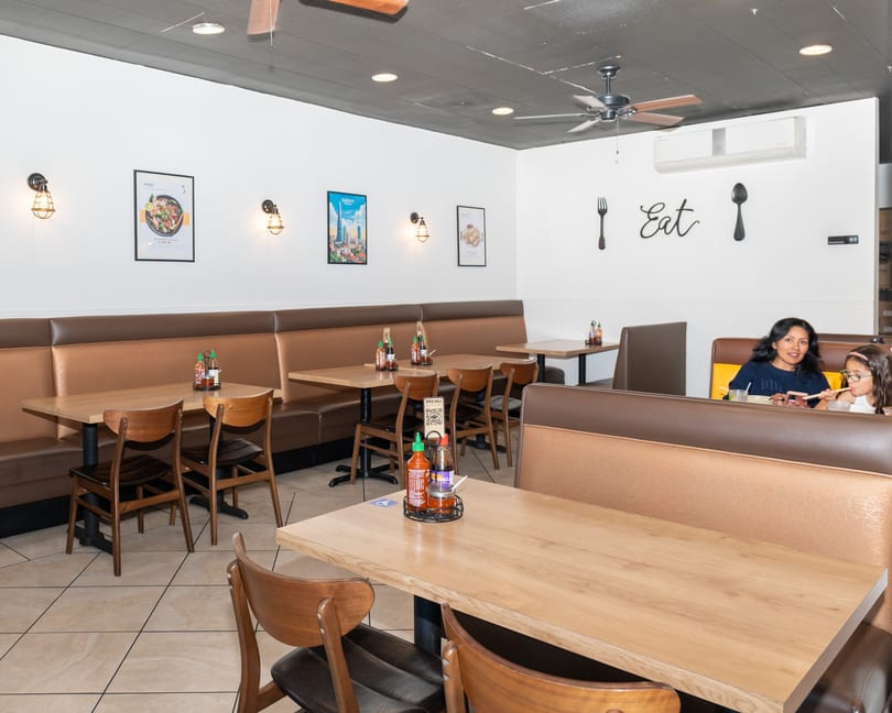 A restaurant interior with brown booths, wooden tables, and a woman and child eating in the background.
